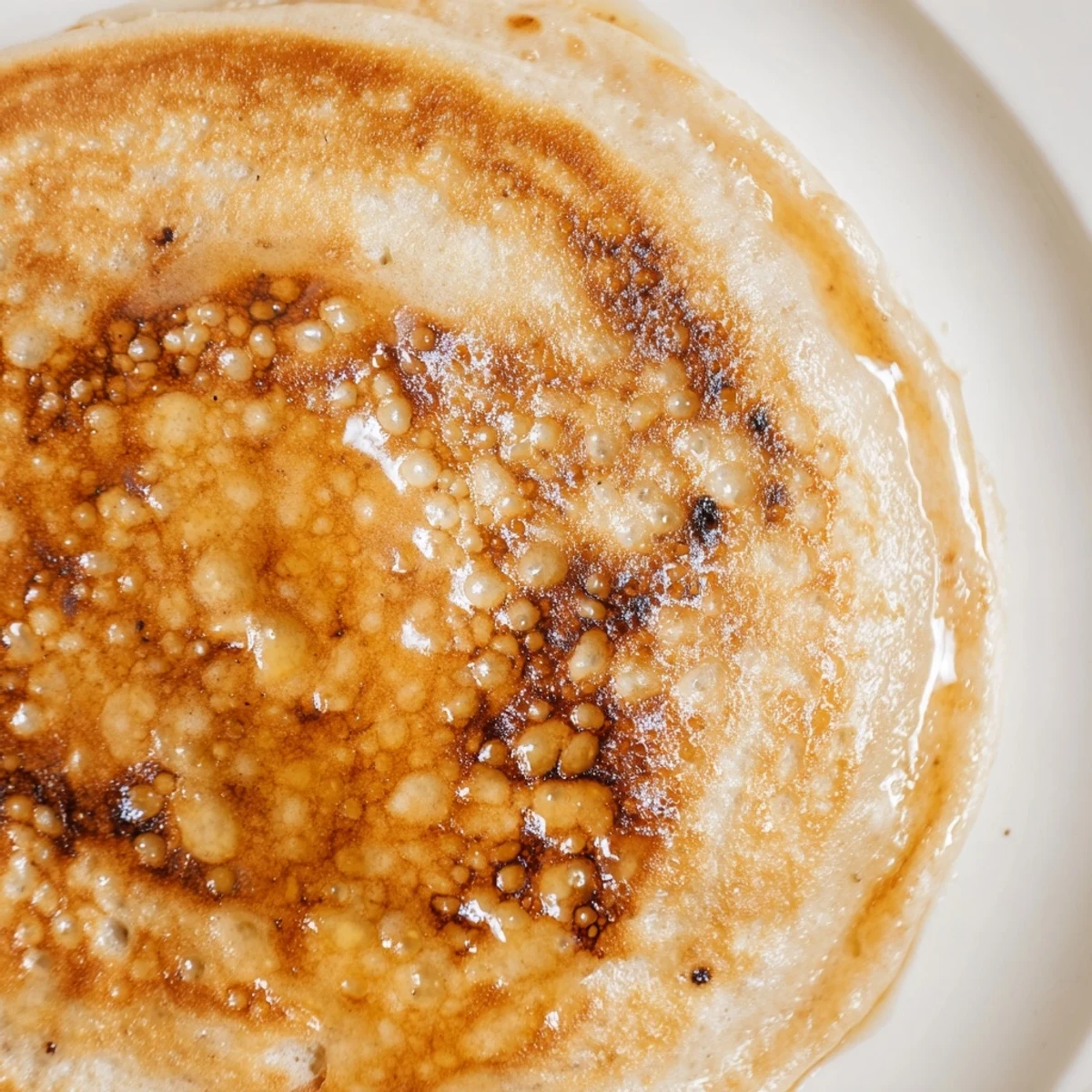 Golden brown banana pancakes glistening with maple syrup sit stacked on a white plate with fresh berries.  