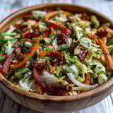 Colorful medley of red cabbage, green cabbage, and bell peppers topped with sun-dried tomatoes and fresh herbs.