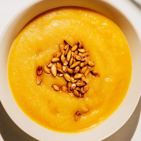 Rich, orange Creamy Roasted Pumpkin Soup with a swirl of cream and crunchy toasted seeds.
