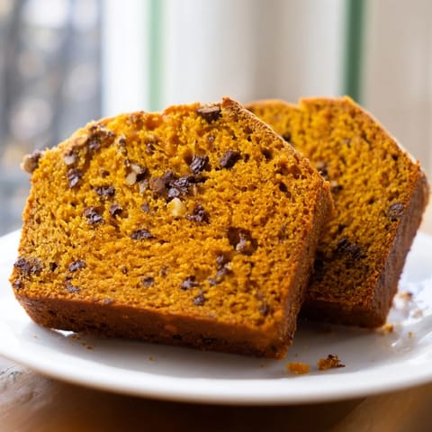 A freshly baked pumpkin loaf rests on a wire cooling rack, its top cracked and dusted with sugar, steam rising gently.  