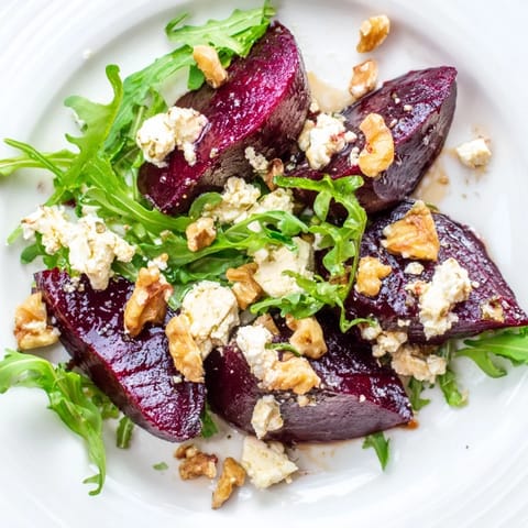 Crisp toasted walnuts and a bright balsamic vinaigrette garnish the vibrant red and green Roasted Beet Goat Cheese Salad in a rustic ceramic bowl.