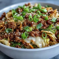 Golden brown ground pork sizzles with ginger and garlic in a skillet, mixed with vibrant shredded cabbage and carrots in this Egg Roll in a Bowl.